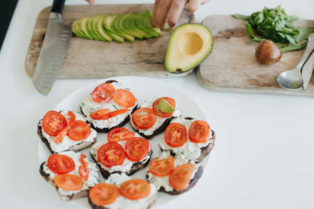 Process of making toasts with avocado on modern white kitchen. Home cooking concept. Hand putting...