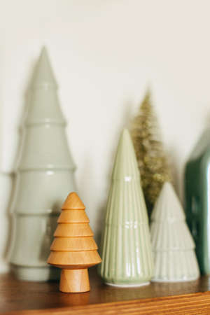 Modern little christmas trees on wooden shelf, stylish festive decor. Christmas miniature forest, wooden and ceramic trees. Merry Christmas and Happy Holidaysの写真素材