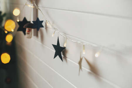 Stylish christmas stars and golden lights bokeh on background of white wall. Decorating festive...