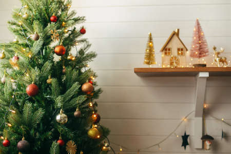 Modern decorated Christmas tree with red and gold baubles and festive lights. Hanging shiny glitter ornaments on christmas tree,  scandinavian room decor for winter holidaysの写真素材