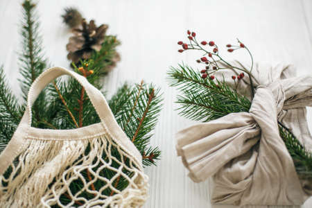 Stylish christmas gift wrapped in linen fabric with green branch and reusable shopping bag with...