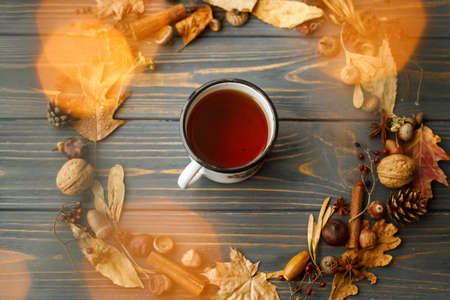 Vintage metal mug with tea and autumn wreath made of leaves, berries, acorns and pine cones on dark...