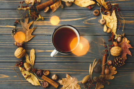 Hello fall! Cozy autumn flat lay. Rustic metal mug with tea and autumn wreath made of leaves, berries, acorns and pine cones on dark wooden background.の写真素材