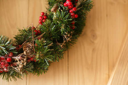 Christmas wreath hanging on rustic wooden door in house.Traditional christmas wreath with red berries and ornaments, pine cones and cinnamon on wooden background, holiday decor.の写真素材