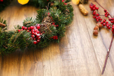 Christmas wreath on wooden rustic background in house.Traditional christmas wreath with red berries and ornaments, pine cones and golden lights on wood, holiday decorの写真素材