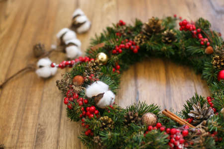 Christmas wreath decorations close up on wooden rustic background. Cotton, red berries, ornaments and pine cones on traditional christmas wreath, holiday workshopの写真素材