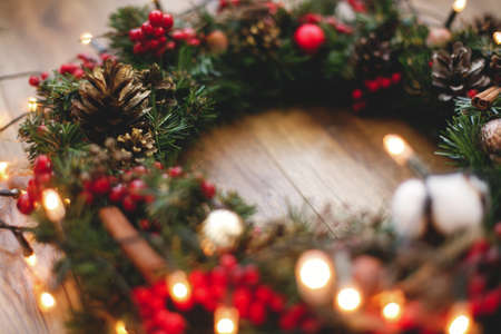 Christmas wreath decorations close up on rustic wood in lights. Cotton, red berries, ornaments and pine cones on traditional christmas wreath, holiday workshop. Space for textの写真素材