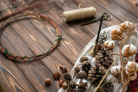Decorations for making rustic christmas wreath. Decorative pine cones, red berries, herbs, twine, cotton and scissors on wooden background. Holiday workshopの写真素材