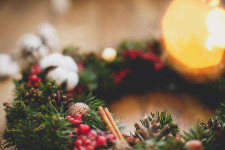 Christmas wreath decorations close up on rustic wood in lights. Cotton, red berries, ornaments and pine cones on traditional christmas wreath, holiday workshop. Space for textの写真素材