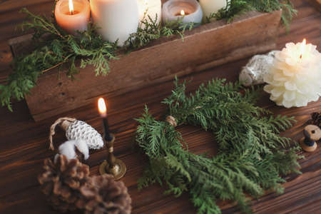 Rustic christmas wreath with candles, pine cones, thread and ornaments on wooden table. Making simple stylish christmas wreath with cedar branches, holiday workshop adventの写真素材