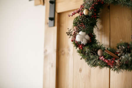 Christmas wreath hanging on rustic wooden door in house.Traditional christmas wreath with red berries and ornaments, pine cones and cinnamon on wooden background, holiday decor. Space for textの写真素材