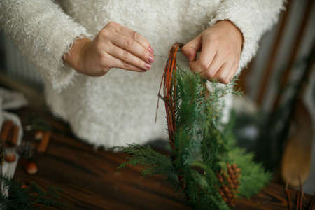 Making rustic christmas wreath, holiday advent. Hands holding green cedar branches on rustic wooden background. Seasonal holiday workshop or making festive decorations at homeの写真素材