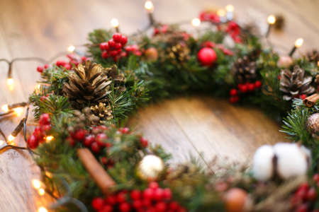 Christmas wreath decorations close up on rustic wood in lights. Cotton, red berries, ornaments and pine cones on traditional christmas wreath, holiday workshop. Space for textの写真素材