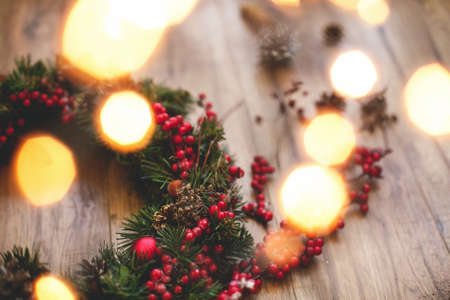 Christmas wreath decorations close up on rustic wood in lights. Red berries, ornaments and pine cones on traditional christmas wreath, holiday workshop. Space for textの写真素材