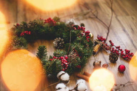 Christmas wreath on wooden rustic background in house.Traditional christmas wreath with red berries and ornaments, pine cones, cotton and golden lights on wood, holiday decorの写真素材