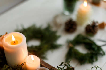 Burning candles on rustic background with christmas wreath, pine cones and ornaments on wooden table in evening. Holiday workshop advent, cozy atmosphere. Copy spaceの写真素材
