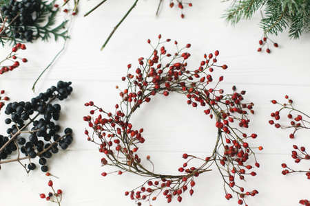 Simple Christmas wreath with red berries on rustic background. Making simple rustic christmas wreath on white wooden table at home, holiday adventの写真素材