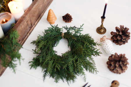 Rustic christmas wreath with candles, pine cones, thread and ornaments on white wooden table. Making simple stylish christmas wreath with cedar branches, holiday workshop adventの写真素材