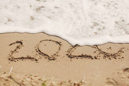 Good bye 2020 ! Wave with foam covering 2020 sign on sandy beach, leaving awful year 2020 behind. Welcoming new year 2021!の写真素材