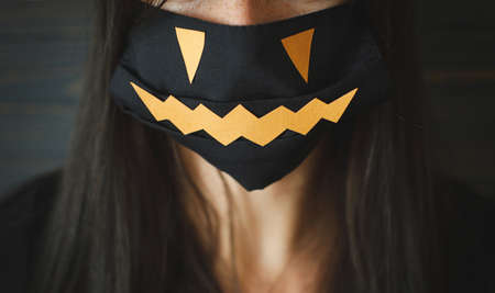 Halloween safe celebration. Young female in black evil face mask close up on dark wooden background. Stay creative, stay safe due coronavirus pandemicの写真素材