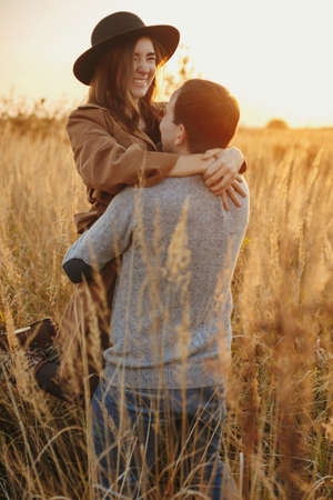 Stylish happy couple dancing in warm sunset light in autumn field. Young fashionable woman and man twirling among grass and herbs in sunshine. Romantic authentic momentの写真素材