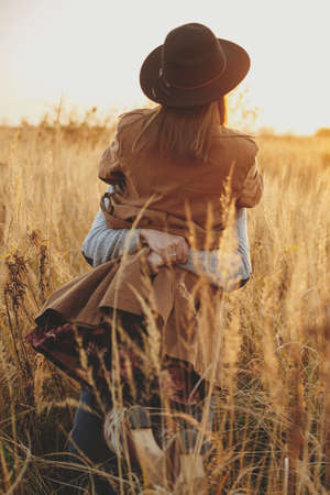 Stylish happy couple dancing in warm sunset light in autumn field. Young fashionable woman and man twirling among grass and herbs in sunshine. Romantic authentic momentの写真素材