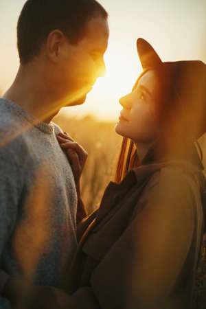 Stylish sensual couple embracing in warm sunset light in autumn field. Young fashionable woman and man gently hugging on background of sunshine. Romantic authentic momentの写真素材