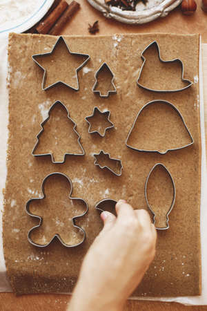 Hands cutting gingerbread dough with festive metal cutters on rustic table flat lay. Person making...
