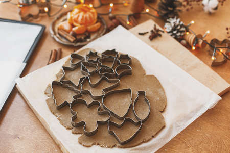 Raw gingerbread dough with festive metal cutters, spices,  decorations and lights on rustic table....