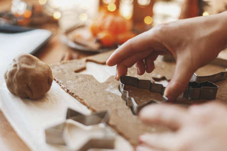 Hands cutting gingerbread dough with christmas tree metal cutter on rustic table with spices,...