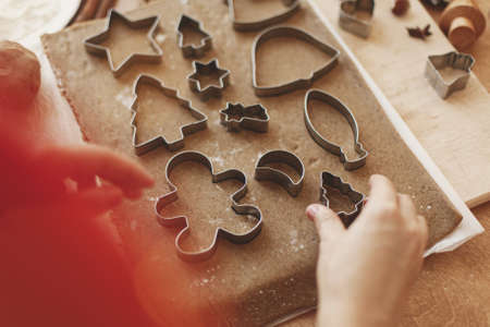 Person making Christmas gingerbread cookies, holiday advent. Hands cutting gingerbread dough with festive metal cutters on rustic table with spices, oranges, festive decorationsの写真素材
