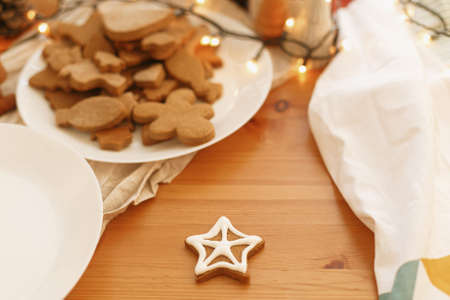 Gingerbread cookies with icing on wooden table with lights. Christmas holiday tradition and advent. Decoratied christmas star cookie with sugar frostingの写真素材