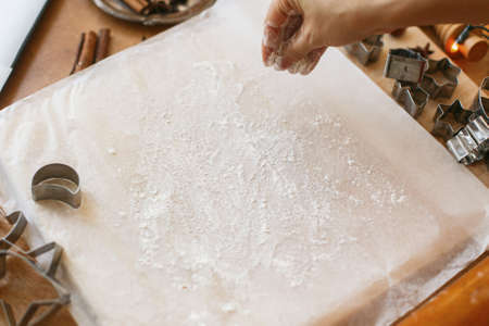 Hands pour flour for kneading raw gingerbread dough on background of metal cutters on rustic table. Person making gingerbread cookies, Christmas holiday traditionの写真素材