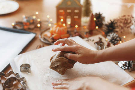 Hands kneading raw gingerbread dough on background of metal cutters, spices, oranges, festive decorations on rustic table. Person making gingerbread cookies, Christmas holiday traditionの写真素材