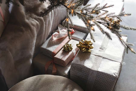 Stylish wrapped christmas gift boxes under christmas tree with golden lights in festive cozy room....