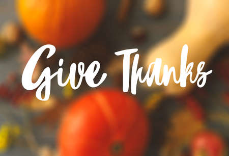 Give Thanks text handwritten on blurred autumn pumpkins, leaves, apples, anise and flowers on dark wood. Seasons greetings. Happy Thanksgiving greeting cardの写真素材