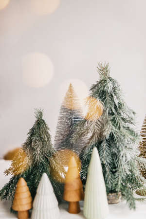 Christmas scene, miniature winter forest in lights. Christmas little ceramic, wooden and snowy pine trees on white background with illumination. Festive modern decoration. Merry Christmas!の写真素材