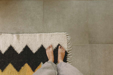 Woman barefoot standing on modern rug in comfortable stylish home, top view. Feet on cozy woolen rug on background of concrete floor. Cozy warm momentsの写真素材