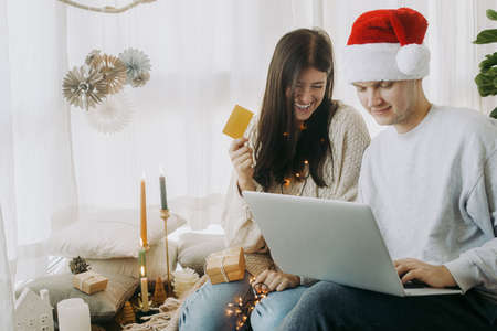 Christmas sales and online home shopping. Happy stylish family  shopping online on Black Friday using laptop and credit card, sitting in modern room with festive holiday decorationsの写真素材