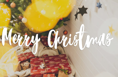 Merry Christmas Greeting card. Merry Christmas text handwritten on stylish christmas gifts under Christmas tree in lights. Modern seasons greetings. Happy holidaysの写真素材