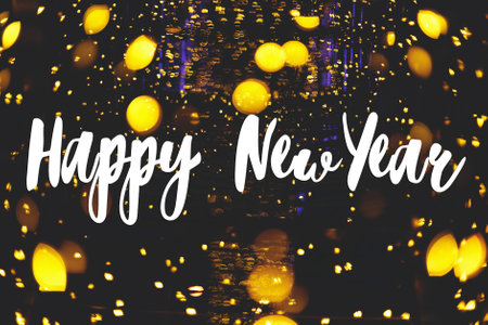 Happy New Year Greeting card. Happy New Year text handwritten on illumination with warm golden lights bokeh, sparkling glitter in holiday evening. Seasons greetings, happy holidaysの写真素材