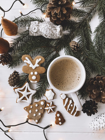 Christmas gingerbread cookies, coffee cup and fir branches on white rustic wooden table with lights. Top view. Happy holidays and Merry Christmas!の写真素材
