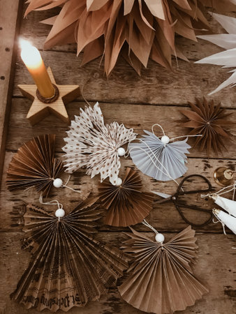 Stylish Christmas paper angels with on rustic wooden table with star candle and metal scissors. Handmade holiday decor, moody imageの写真素材