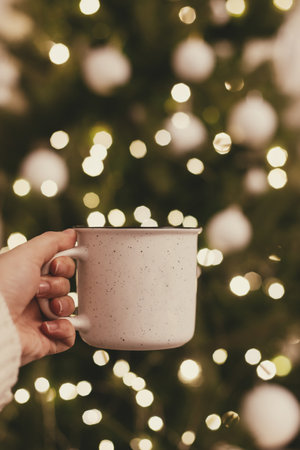 Hand holding festive cup of tea on background of Christmas tree lights bokeh. Merry Christmas and Happy Holidays!の写真素材