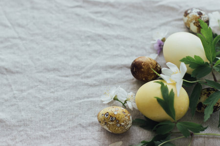 Easter eggs with spring flowers on rustic linen background with space for text.  Aesthetic seasons greeting card. Stylish modern easter and quail eggs in natural dye and spring blooms.の写真素材