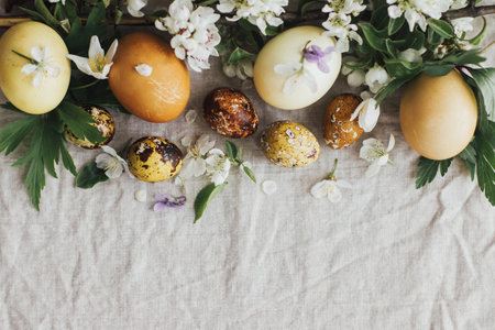 Easter eggs with spring flowers on rustic linen background, flat lay with space for text. Stylish modern easter and quail eggs with natural dye and spring blooms. Aesthetic seasons greeting cardの写真素材