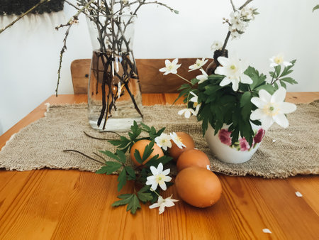 Easter eggs with spring flowers on wooden rustic table in room at home. Natural eggs, cherry blooms...