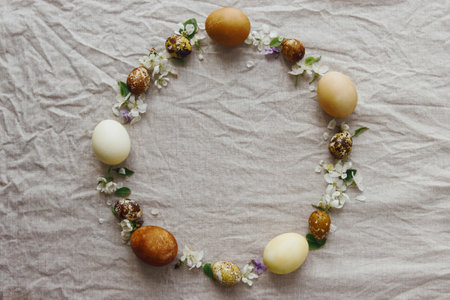 Happy Easter! Easter eggs and spring flowers in wreath on rustic linen, flat lay with space for...