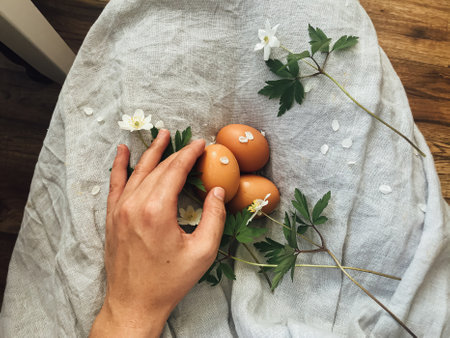 Hand holding natural easter eggs and spring flowers on background of rustic linen dress. Happy Easter! Woman holding natural eggs. Aesthetic holiday, top viewの写真素材