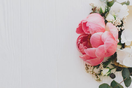 Happy mothers day and valentines day. Creative floral greeting card. Peony, white flowers and eucalyptus growing from craft envelope on white wood with space for text. Flower delivery